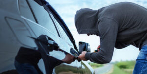 car thief in action, a man in a hood breaks a screwdriver car door